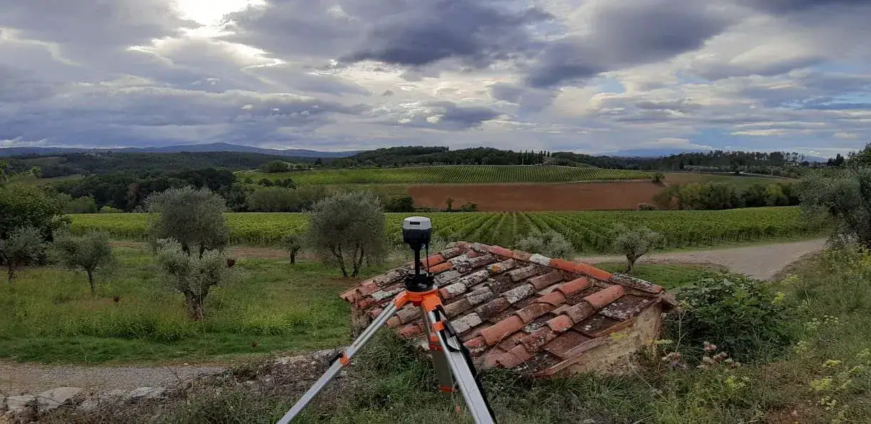 Un ricevitore satellitare su un treppiede arancio, sopra un tetto di coppi, fra olivi e vigne