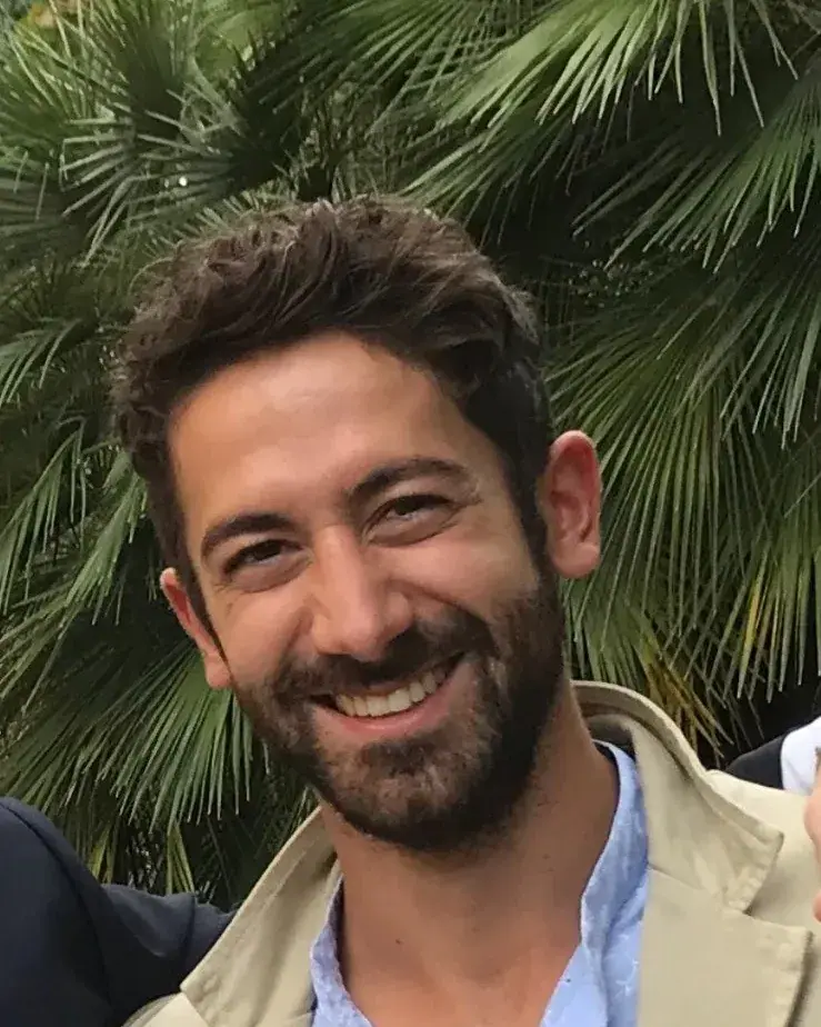 Gian Marco Aminti sorride, con una giacca chiara, fra le palme